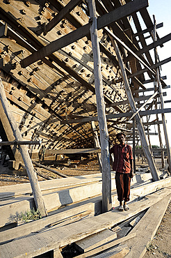 Boatbuilder beneath the hull of ocean going dhow under construction by hand from Sal wood, Rukmavati River, Mandvi, Gujarat, India, Asia