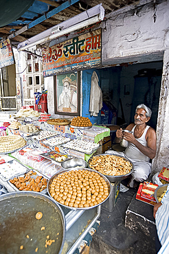 Diwali sweet stall with stallholder and picture of the Hindu god, Hanuman, Udaipur, Rajasthan, India, Asia