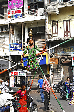 Young girl performing on a tightrope erected in a busy street to earn money, old Ahmedabad, Gujarat, India, Asia