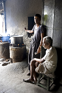 Young man stirring milk for chai, with blind man sitting beside him, roadside chai stall, Dangiyawas, Rajasthan, India, Asia