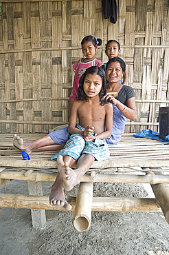 Mishing tribeswoman combing her daughter's hair on the verandah of their family home, Majuli Island, Assam, India, Asia