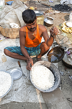 Man in vest and dhoti pouring sugar syrup onto bowl of puffed rice to make prasad, Sonepur Cattle Fair, Bihar, India, Asia