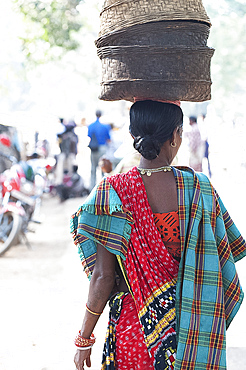 Woman at weekly tribal market wearing brightly coloured clothing and carrying baskets on her head, Bissam Cuttack, Orissa, India, Asia