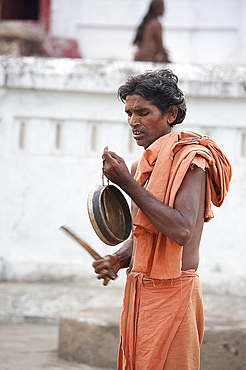 Joranda monk at dusk, wearing orange cloth, sounding a cymbal as preparation for ritual evening prayer, Joranda, Orissa, India, Asia