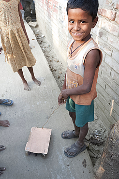 Young smiling village boy with wheeled toy vehicle pulled on piece of wire, in a village street, rural West Bengal, India, Asia