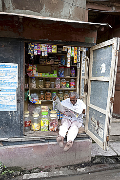 Shop owner reading the newspaper in the morning, Kolkata, West Bengal, India, Asia