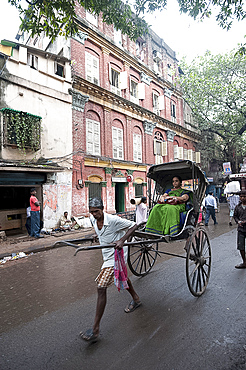 Woman riding in running rickshaw passing beautiful old Raj era Kolkata building in Kolkata backstreet, West Bengal, India, Asia