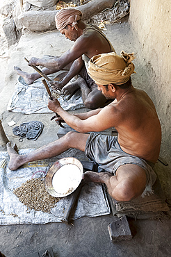 Two men smoothing surface of rough cast brass dishes outside village foundry, Hirapur, Orissa, India, Asia