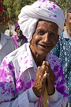 Man offering Namaste greeting on his way back from village wedding celebrations where watered pink dyed powder has been thrown, Ajmer district, Rajasthan, India, Asia