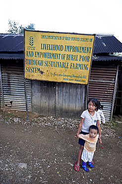 Naga village children beneath a local government sign for livelihood improvement through sustainable farming, rural Nagaland, India, Asia