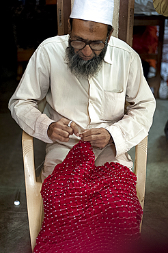 Muslim man, skilled bhandani tie-dye master, tying precise small knots in red silk, in preparation for second colour dyeing, Mandvi, Gujarat, India, Asia