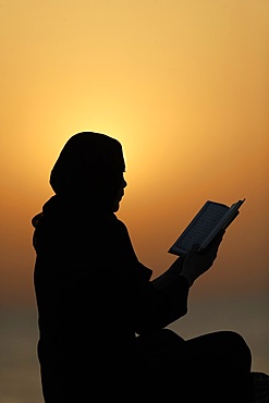 Silhouette of a Muslim woman reading the Noble Quran at sunset, United Arab Emirates, Middle East