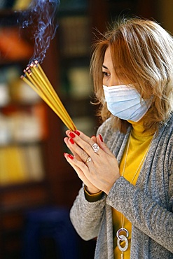 Woman wearing surgical mask praying with incense sticks, Tu An Buddhist Temple, Haute Savoie, France, Europe