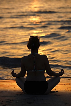 Woman practising yoga meditation on beach at sunset as concept for silence and relaxation, United Arab Emirates, Middle East