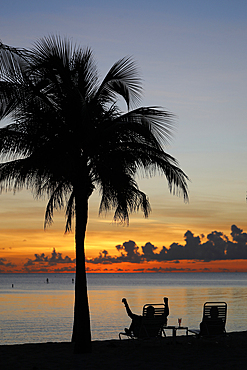 Retired man sitting on a chair at sunset, tropical beach and paradise nature, Cayman Islands, Caribbean, Central America