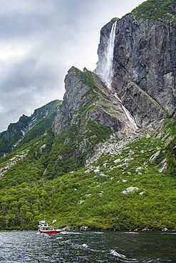 Little tourist boat under the Pissing Mare Falls in the western Brook Pond, Gros Morne National Park, UNESCO World Heritage Site, Newfoundland, Canada, North America