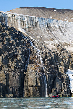 Tourist in a zodiac looking at Waterfall dropping in the ocean, Alkerfjellet, Svalbard, Arctic