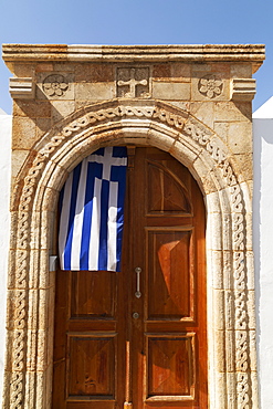 A Greek flag hangs under the stone archway in the doorway of one of the captain's houses of Lindos on Rhodes, Dodecanese, Greek Islands, Greece, Europe