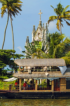 Old church with patinated facade and moored houseboat on a backwaters cruise visitor stop, Alappuzha (Alleppey), Kerala, India, Asia