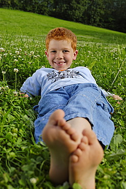 Boy lies barfoot in a meadow