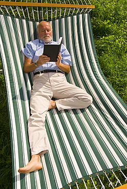 Elderly gentleman lying in a hammock reading a book