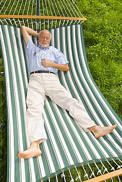 Elderly gentleman lying in a hammock and listening to music