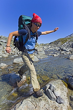 Young woman jumping across a creek, hiking, backpacking, hiker with backpack, historic Chilkoot Trail, Chilkoot Pass, near Crater Lake, alpine tundra, Yukon Territory, British Columbia, B. C., Canada