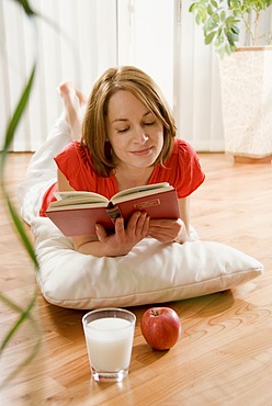 Woman laying on a parquet floor reading a book