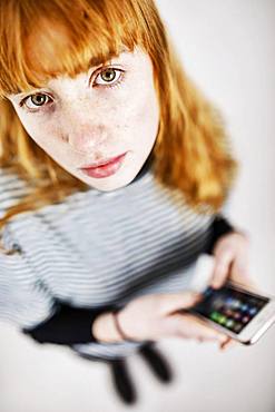 Girl, teenager, with smartphone in hand, looks thoughtfully into camera, studio shot, Germany, Europe