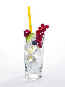 Glass prepared for cocktail, decorated with raspberry, blueberry, lime and red currant, drinking straw, ice cubes, Germany, Europe