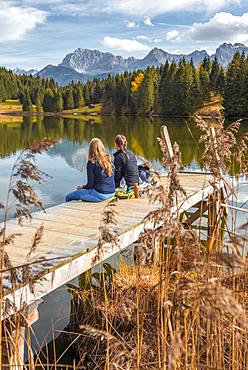 Two young women sitting at a jetty having a snack, Lake Geroldsee, Mittenwald, Karwendel, Bavaria, Germany, Europe