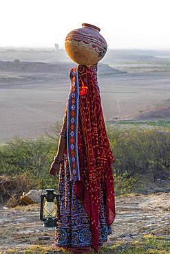 Ahir woman in traditional colorful clothes carrying water in a clay jug on her head, Great Rann of Kutch, Gujarat, India, Asia