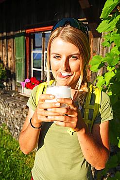 Young female hiker drinks buttermilk at the Kraftalm, Hohe Salve, Itter, Kitzbuehel Alps, Tyrol, Austria, Europe