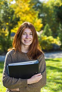 Young smiling red-haired woman, student, pupil holds folder, Bavaria, Germany, Europe