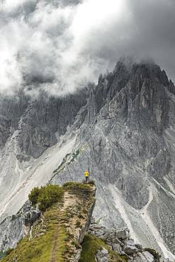 Woman in yellow jacket standing on a ridge, behind her mountain peaks and sharp rocky peaks, dramatic clouds, Cimon the Croda Liscia and Cadini group, Auronzo di Cadore, Belluno, Italy, Europe