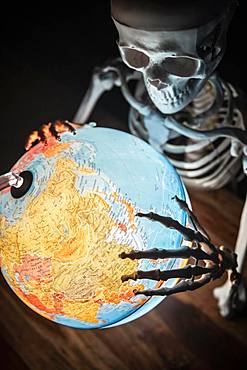 Skeleton with bony hand on globe, symbolic image of war and environmental catastrophe, Germany, Europe