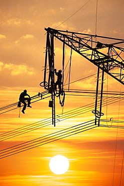 High voltage fitters working on the high voltage pylon at sunset, Baden-Wuerttemberg, Germany, Europe