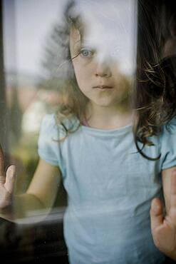 Child looks sadly through window pane