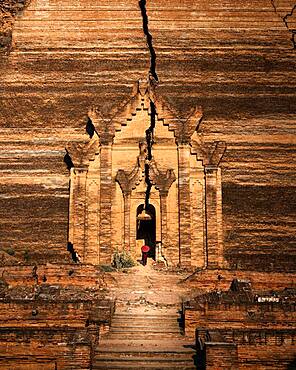 Buddhist monk stands with red umbrella in the entrance of Mingun Pagoda, Mingun, Myanmar, Asia