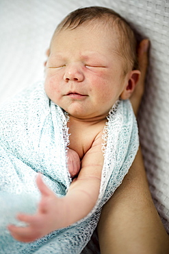 Cute sleeping newborn baby boy wrapped in blue laying on mother's hand