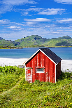 Rorbuer, traditional wooden house on sandy beach Rambergstranda, mountains and sea, Junesvika, Lofoten, Nordland, Norway, Europe