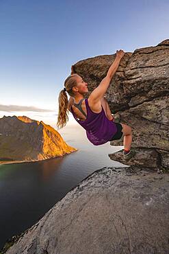 Evening atmosphere, Young woman bouldering, Climbing, Peak of Ryten, Sea, Kvalvika beach and mountains, Fredvang, Lofoten, Nordland, Norway, Europe