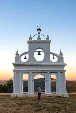 Bell ringer ringing the bells at the bell tower of the chapel Ermita Reina de los Angeles, at sunset, Alajar, Huelva, Spain, Europe