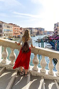 Young woman with red skirt walks over a bridge at the Grand Canal, Rialto Bridge, Venice, Veneto, Italy, Europe