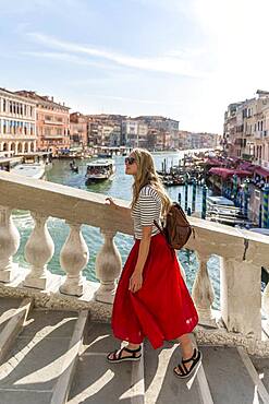 Young woman with red skirt walks over a bridge at the Grand Canal, Rialto Bridge, Venice, Veneto, Italy, Europe