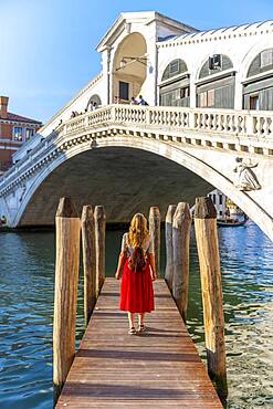 Young woman with red dress at a pier with boats, Grand Canal, Rialto Bridge, Venice, Veneto, Italy, Europe