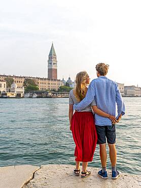 Young couple standing by the sea enjoying view of St. Mark's Square with Campanile di San Marco, Venice, Veneto, Italy, Europe