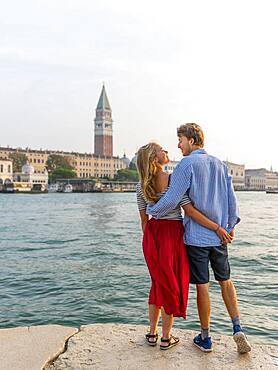 Young couple in love standing by the sea enjoying view of St. Mark's Square with Campanile di San Marco, Venice, Veneto, Italy, Europe