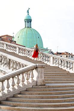 Young woman with red skirt walks over a bridge at the Grand Canal, church San Simeone Piccolo, Ponte degli Scalzi, Venice, Veneto, Italy, Europe