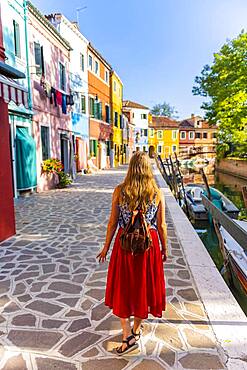 Woman walking past colorful houses, canal with boats and colorful house facades, Burano Island, Venice, Veneto, Italy, Europe